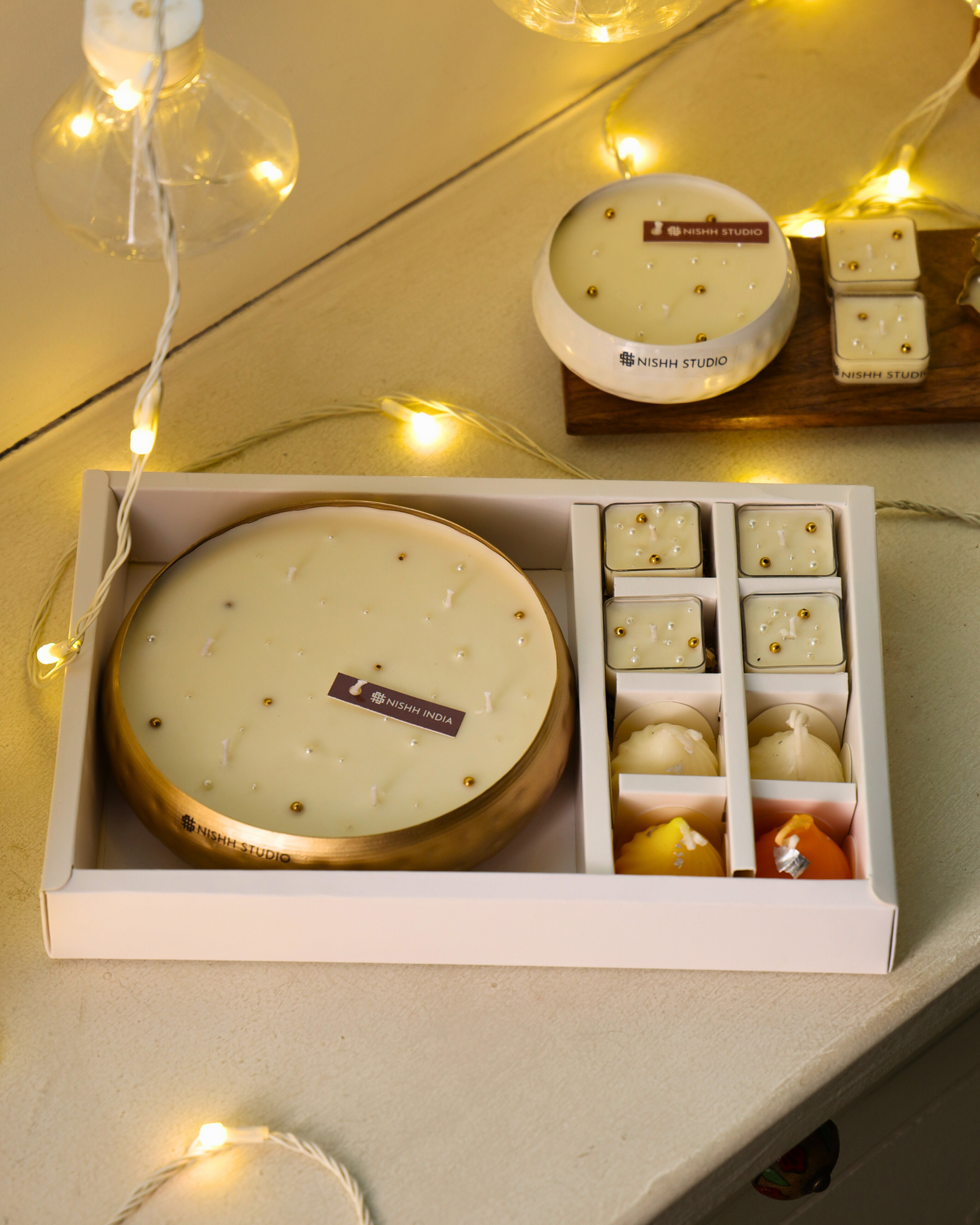 Set of candles in a box with decorative lights on a wooden surface