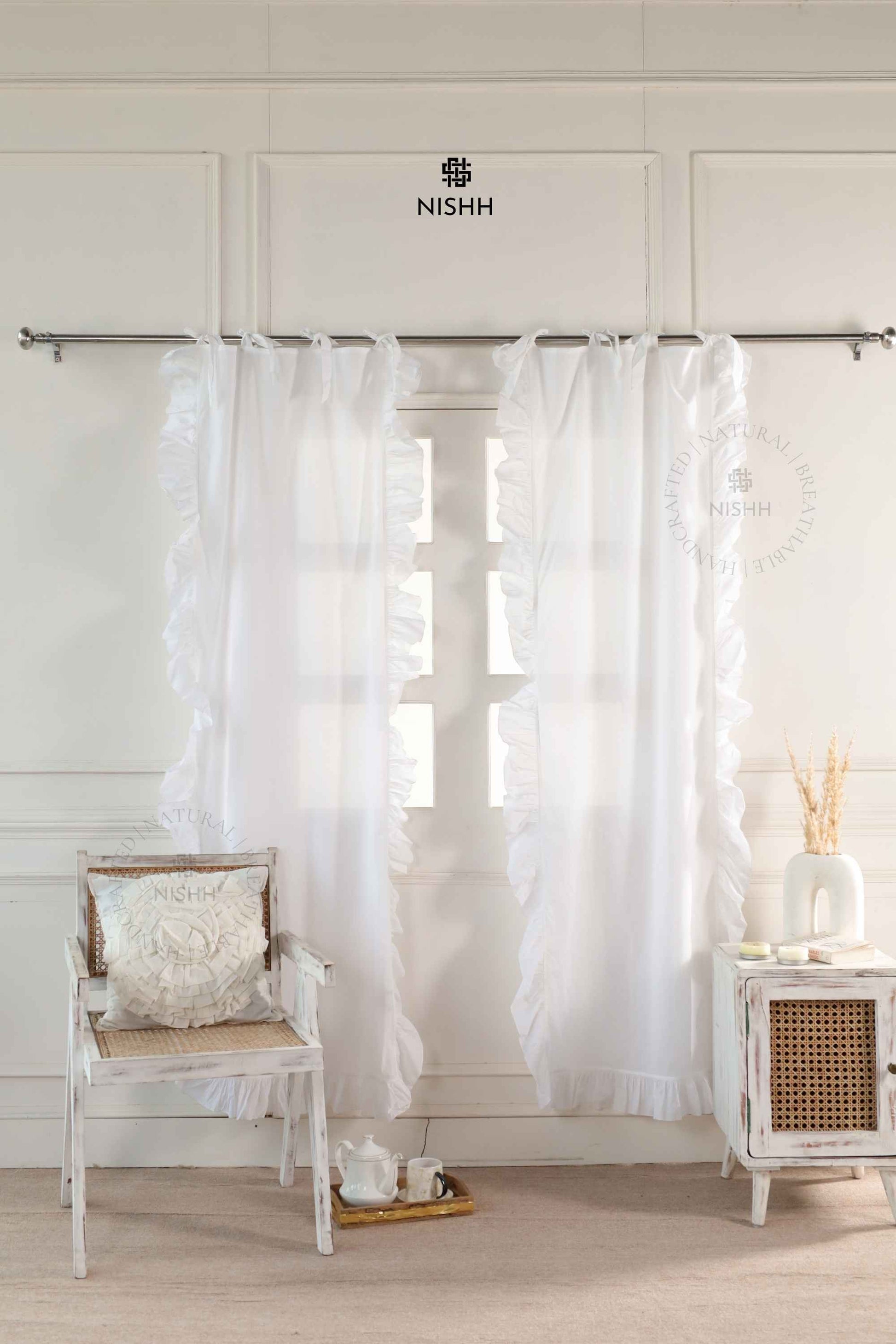 White curtains hanging in a room with a chair and small table, featuring the Nishh brand.