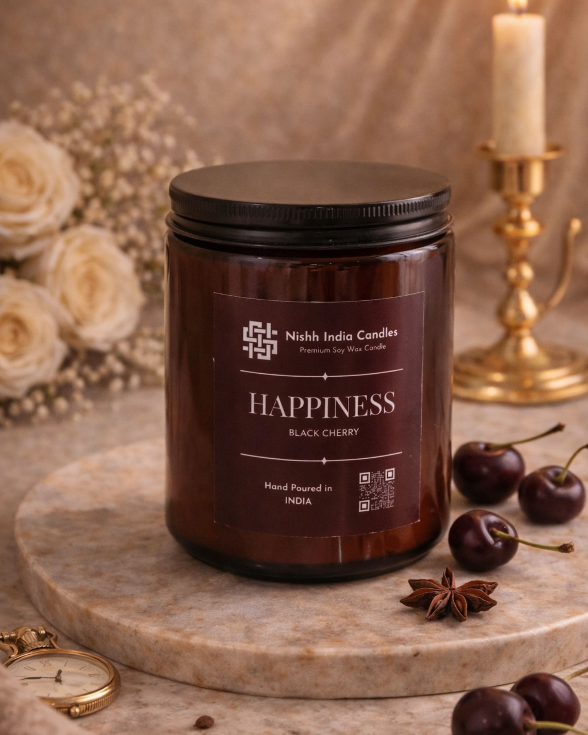 Nishh India Happiness Black Cherry scented soy wax candle in amber glass jar styled in luxury setting with cherries, warm candlelight and elegant home decor backdrop.