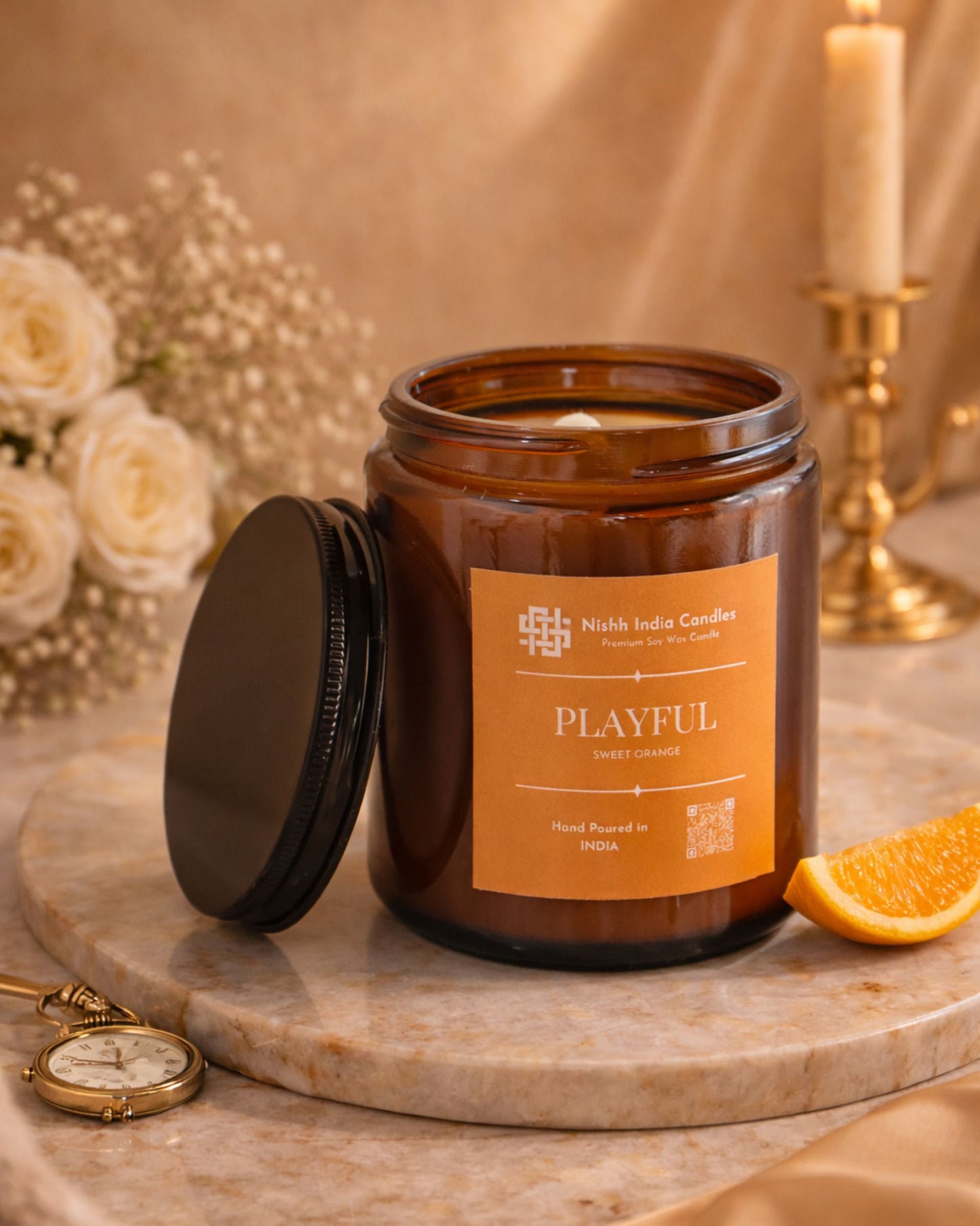 Nishh India Playful Sweet Orange premium soy wax candle in amber glass jar styled on marble base with orange slices, star anise and warm luxury decor background