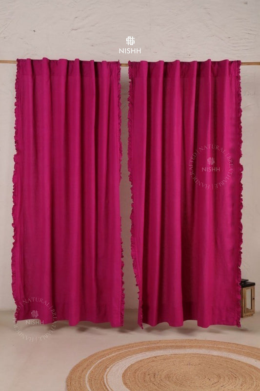 Pair of pink curtains with lace trim on a wooden rod against a light-colored wall.